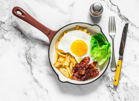 Delicious brunch, breakfast - potatoes hash, fried egg, bacon and green salad in a frying pan on a light background, top viewの写真素材