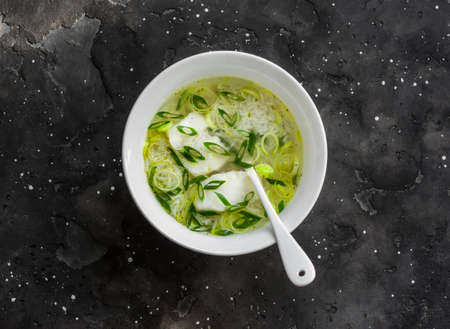 Cod, leek and rice broth on a dark background, top view. Delicious soup for lunchの写真素材