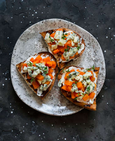 Delicious appetizer, tapas - baked pumpkin, gorgonzola, honey, thyme bruschetta on a dark...