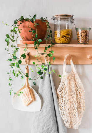 Scandinavian kitchen interior - wooden shelf-hanger on a gray wall with a flower, a jar of dry pasta, granola and linen towels. Eco style interiorの写真素材