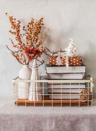 Metal vintage basket with books, dried flowers, ceramic Christmas decorations, gift box on the table in a cozy interiorの写真素材