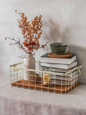 Cozy simple home interior - books in a metal basket, a ceramic cup, dried flowers in a vase on the table. Cozy home interior conceptの写真素材