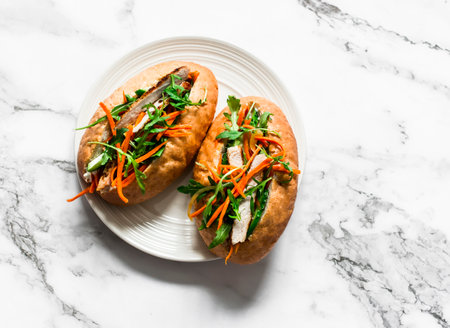 Delicious asian style hot dog - bun with fried pork, cucumber, spicy carrots and arugula on a light background, top viewの写真素材