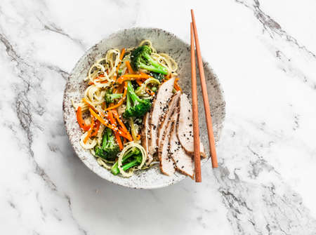 Noodles with vegetable stir fry and roasted chicken breast on a light background, top view....