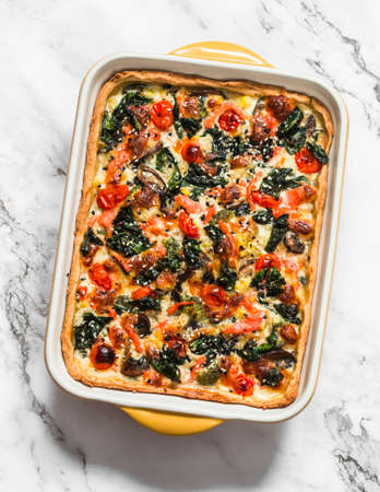 Savory pie with salmon, mushrooms, vegetables, spinach and cheese in a baking dish on a light...