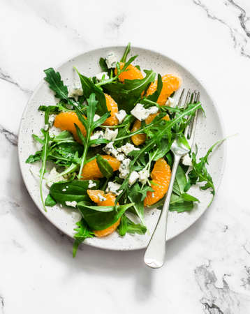 Fruit salad with tangerines, green salad mix and gorgonzola on a light background, top viewの写真素材