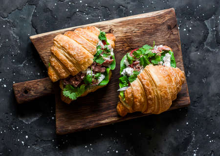 Canned tuna, cream cheese, tomato, lettuce croissants sandwiches on rustic cutting board on a dark background, top viewの写真素材