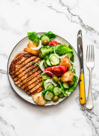 Grilled pork chop and Italian panzanella salad on a light marble background, top viewの写真素材