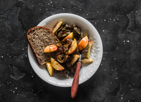 Fried chicken liver with onions and apples in a bowl on a dark background, top viewの写真素材