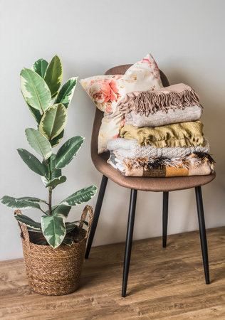A chair with a stick of warm cozy autumn blankets, plaids, a basket with a ficus in the interior of the living roomの写真素材