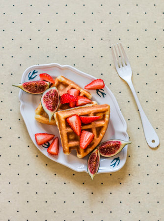 Waffles with figs and strawberries on a light background, top view