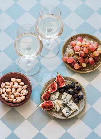 Appetizer, aperitif, tapas - glasses of white wine, red grapes, figs, gorgonzola, pistachios on a light background, top viewの写真素材