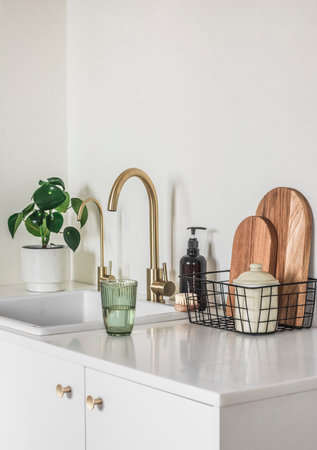 Beautiful bright interior of the kitchen in a minimalist style - kitchen furniture with ceramic sink, brass faucet, cutting boards, kettle and homemade flower on the surfaceの写真素材
