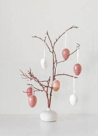 Creative Easter bouquet - pink eggs on branches in a ceramic vase on a light background. easter...