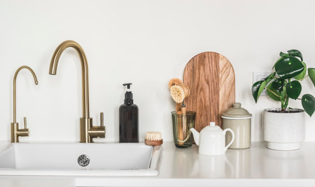 Minimalism interior of the kitchen - kitchen furniture with ceramic sink, brass faucet, cutting boards and home flower on the white surfaceの写真素材