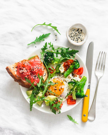 Delicious sandwich - wholegrain toast with poached egg, cherry tomatoes, avocado and arugula on a light background, top viewの写真素材