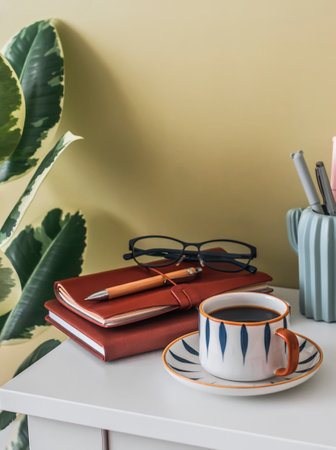 Coffee break at home office. A cup of coffee, notebooks, stationery, glasses on the desktopの写真素材