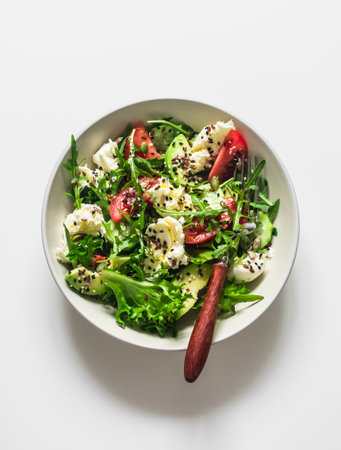 Simple salad with fresh vegetables, avocado and mozzarella on a light background, top view