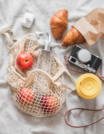 Summer picnic place - croissants, fruit, camera, coffee in a thermocup on a gray blanket, top view
