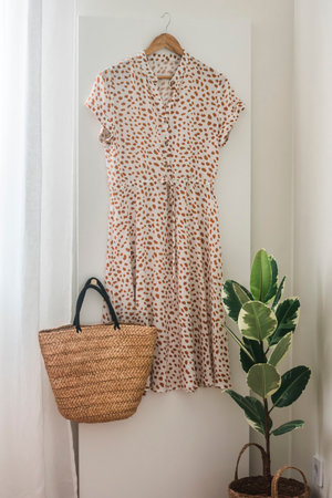 Women's summer dress, straw bag on a hanger in a cozy roomの写真素材