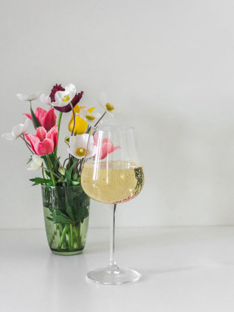 A glass of white wine and a bouquet of spring flowers on a white tableの写真素材