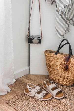 Hotel entrance hall interior. Straw basket, women's sandals, beach towel, camera, jute mat on wooden floorの写真素材