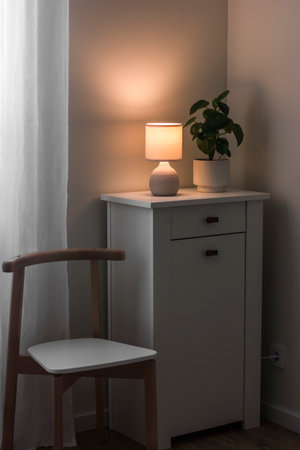 Cozy evening - ceramic lamp on the dresser, home flower, chair. Scandinavian style interiorの写真素材