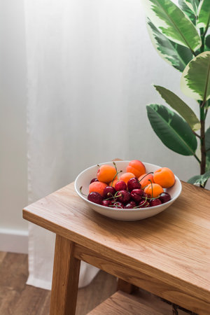 A bowl with seasonal summer fruits and berries on a wooden oak bench in a cozy living roomの写真素材