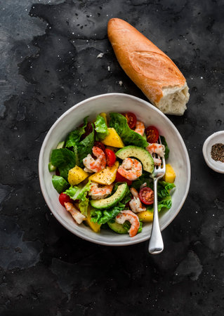 Delicious avocado, mango, shrimp, tomato salad and crispy baguette on a dark background, top viewの写真素材