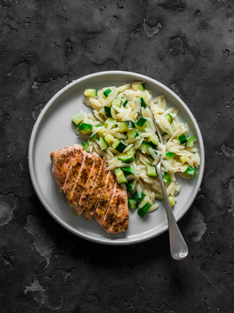 Delicious lunch - pasta orzo with zucchini and roasted chicken breast on a dark background, top viewの写真素材