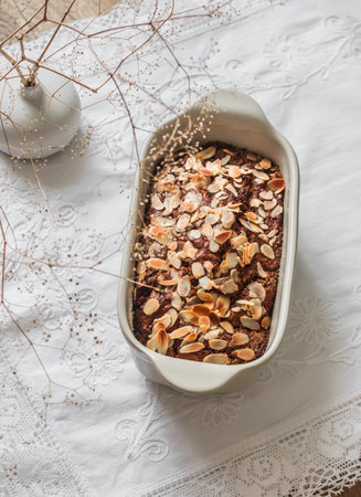 Chocolate oatmeal banana cake decorated with almond petals in a ceramic baking dish on a light...
