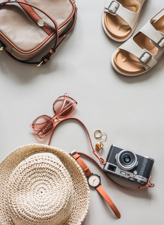 Summer women's accessories - comfortable sandals, straw hat, retro camera, sunglasses, wristwatch on a light gray background, top viewの写真素材