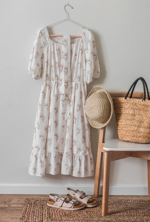 Women's linen dress in retro style on a hanger, sandals and straw hat and bag on a chair in the bedroom interiorの写真素材