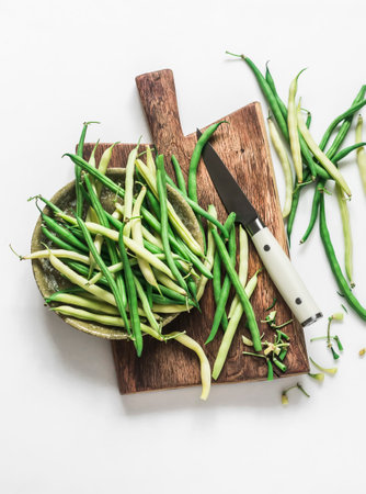 Green and yellow string beans on a wooden chopping board on a light background, top viewの写真素材