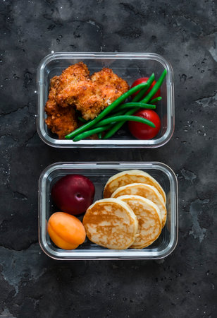 School lunch box - containers with nuggets, green beans, pancakes and fruit on a dark background, top viewの写真素材