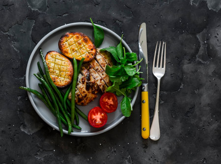 Grilled plate - turkey fillet, potatoes, green beans, arugula on a dark background, top viewの写真素材