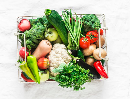Basket with an abundant autumn seasonal harvest of vegetables - pumpkin, cauliflower, broccoli, string beans, squash, potatoes, tomatoes on a light background, top viewの写真素材