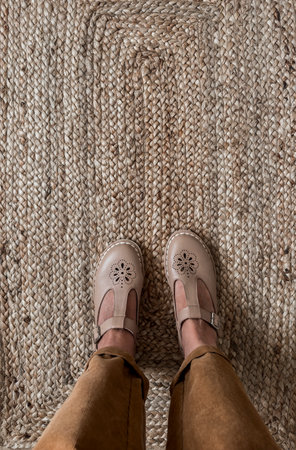 Women's feet in comfortable retro leather sandals and corduroy trousers on a jute carpet, top viewの写真素材