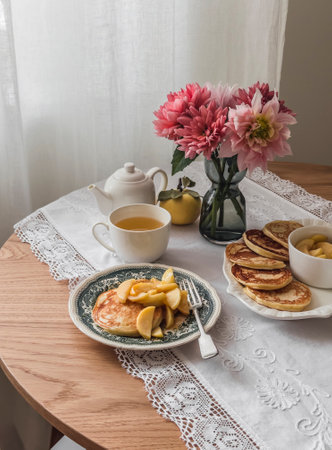 Cozy breakfast - pancakes with apple sauce, green tea, a bouquet of autumn flowers on a wooden table in a cozy living roomの写真素材