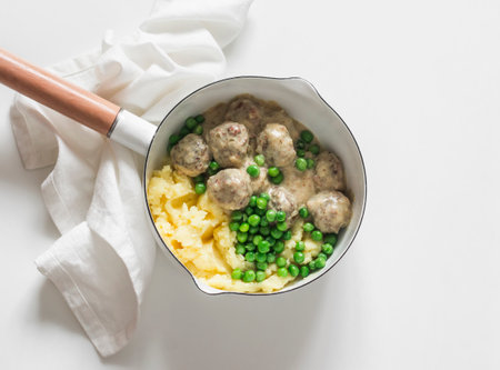 Delicious homemade lunch - mashed potatoes, Swedish meatballs in cream sauce and green peas in a saucepan on a light background, top viewの写真素材