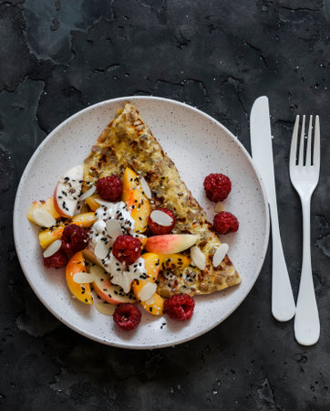 Oatmeal pancake made of whole grain flakes and eggs with fruits, berries and Greek yogurt on a dark background, top viewの写真素材