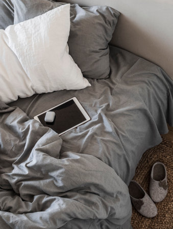 Lazy weekend concept. Tablet in a bed, top view. Scandinavian style bedroom