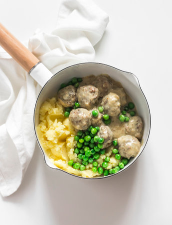 Delicious homemade lunch - mashed potatoes, Swedish meatballs in cream sauce and green peas in a saucepan on a light background, top viewの写真素材