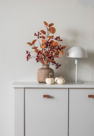 Autumn bouquet in a ceramic vase, scandinavian style table lamp, decorative pumpkins on a white chest of drawersの写真素材