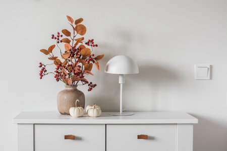 Autumn bouquet in a ceramic vase, scandinavian style table lamp, decorative pumpkins on a white chest of drawersの写真素材