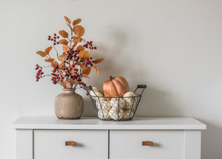 Autumn decor on the dresser in the living room - a bouquet of autumn leaves and berries and a basket with pumpkinsの写真素材