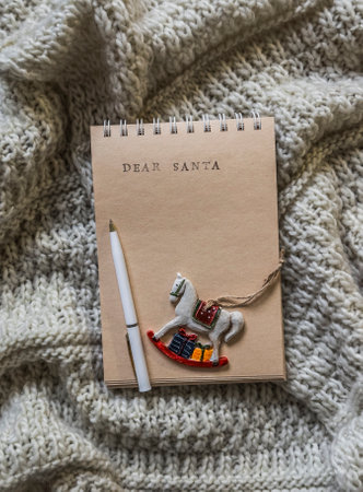 Notebook with a letter to Santa Claus, retro Christmas toy horse on a knitted blanket, top viewの写真素材