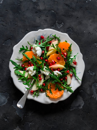 Rocket salad with tangerines, pomegranate, apples and mozzarella cheese on a dark background, top viewの写真素材