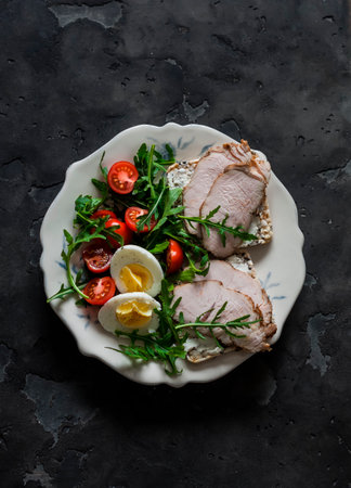 Delicious diet lunch, breakfast, snack - turkey sandwich, boiled egg, vegetables arugula salad on a dark background, top viewの写真素材