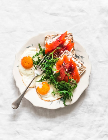 Breakfast, brunch plate - fried eggs, arugula salad, crispy bread curd cheese smoked salmon sandwiches on a light background, top viewの写真素材